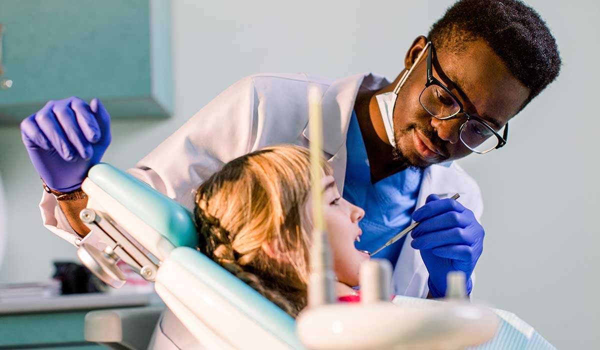 A dentist works on a young child as she smiles