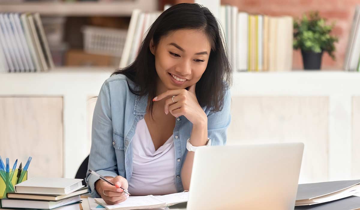 A young woman takes notes while looking at a laptop computer