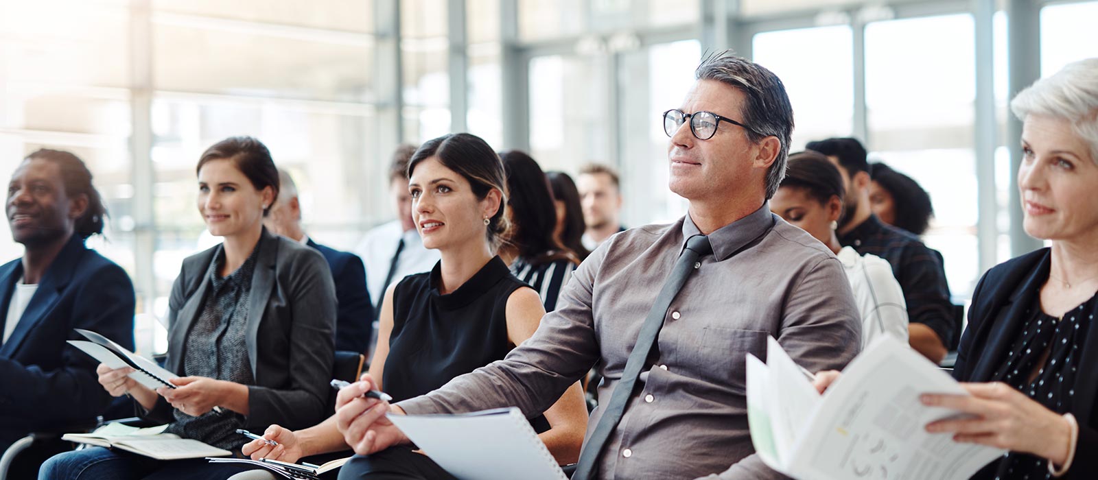 A group of attentive listeners take notes in a conference room