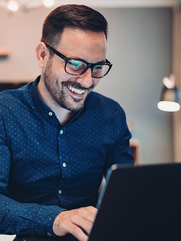 A man smiles while typing on a computer laptop